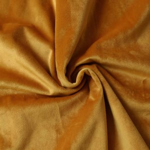 May include: Close-up of a soft, golden yellow velvet fabric. The fabric is draped and folded, showcasing its texture and luxurious feel.
