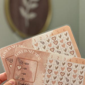 May include: Two pink and brown cards with the text "Love is Neutral" and a grid of hearts and leaves. The cards have a price list for different colored hearts: $10, $5, $4, and $3.