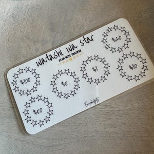 May include: A white sheet with black star-shaped circles and the text "watashi wa star STAR NOTE TRACKER" and dollar amounts in each circle: £100, £50, £5, £1, £20, and £10.