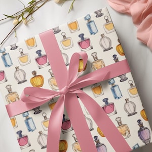 May include: A white gift box with a pink ribbon tied in a bow. The box is wrapped in paper with a repeating pattern of colourful perfume bottles.