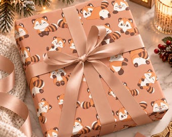Puede incluir: Una caja de regalo cuadrada envuelta en papel color melocotón con un patrón repetitivo de pandas rojos de dibujos animados con colas a rayas. La caja está atada con una cinta de satén a juego en un lazo central.