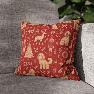 Puede incluir: Cojín decorativo rojo con un patrón repetido de ilustraciones doradas con temática navideña. El diseño incluye renos, perros, árboles de Navidad, cascanueces, lazos y ramitas. El cojín es cuadrado.