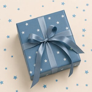 May include: A square gift box wrapped in blue paper featuring a white star pattern. The box is tied with a smooth, matching blue satin ribbon that is knotted into a decorative bow on the top center, creating a clean and festive presentation.