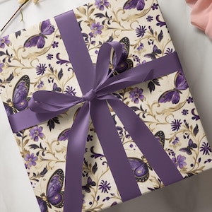 May include: Square gift box wrapped in cream-colored paper with a butterfly and floral pattern in purple and gold. A wide purple satin ribbon is tied in a bow around the box. The box is on a white marble surface.