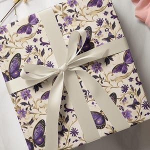 May include: A square gift box wrapped in cream-colored paper with a repeating pattern of purple butterflies and flowers. A cream-colored satin ribbon is tied in a bow around the box.