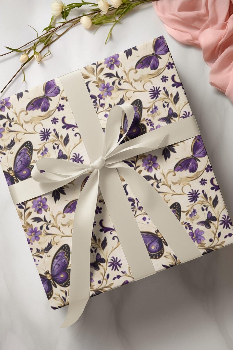 May include: A square gift box wrapped in cream-colored paper with a repeating pattern of purple butterflies and flowers. A cream-colored satin ribbon is tied in a bow around the box.