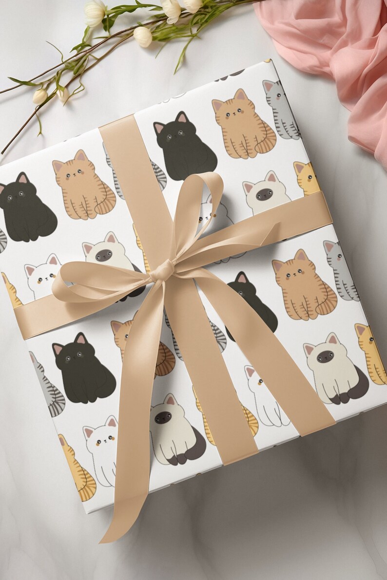 White gift wrap with a repeating pattern of cute cartoon cats in various colours and poses. The gift wrap is tied with a brown satin ribbon.