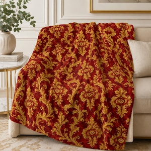 May include: A plush throw blanket featuring a deep red background with a repeating golden yellow damask pattern. The fabric displays intricate, swirling acanthus leaf motifs arranged in a symmetrical, ornate design across the entire surface.