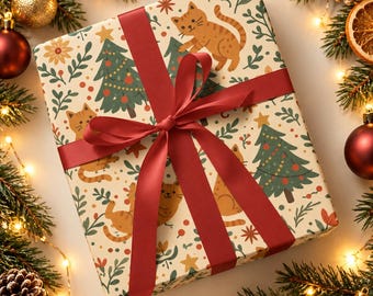 May include: A square gift box wrapped in cream-colored paper featuring a repeating pattern of orange tabby cats, green Christmas trees, red berries, and small yellow stars, tied with a wide, dark red satin ribbon bow.