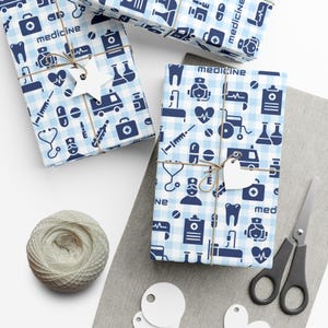 Blue and white wrapping paper with a medical theme. The paper features a variety of medical symbols, including a stethoscope, a syringe, a pill bottle, a thermometer, and a first aid kit. The paper also includes the word "medicine" repeated throughout.