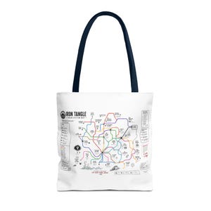 May include: White tote bag with a navy blue handle featuring a colorful map design. The map includes various colored lines and icons, with the text "IRON TANGLE - TRAIN SYSTEM MAP" and "EAT. SLEEP. CRAWL. REPEAT."