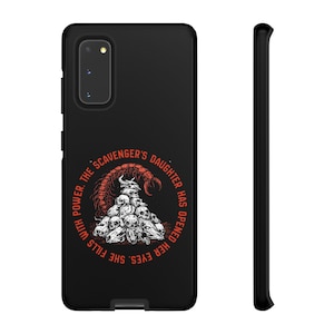 May include: A black smartphone case featuring a graphic of a scorpion tail arching over a pile of skulls. The text "THE SCAVENGER'S DAUGHTER HAS OPENED HER EYES. SHE FILLS WITH POWER." is printed in orange in a circular pattern around the illustration.