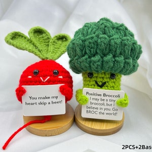 Peut inclure: Deux peluches en crochet, un radis rouge et un brocoli vert, tenant des pancartes avec des messages. Le radis dit "You make my heart skip a beet!" et le brocoli dit "Positive Broccoli I may be a tiny broccoli, but I believe in you. Go BROC the world!" Ils sont tous les deux sur des bases en bois.