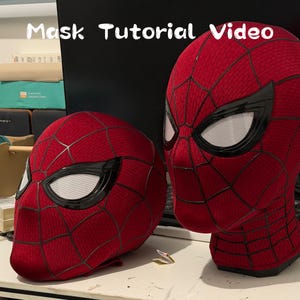 May include: Two red fabric masks with a black web pattern and large white mesh eye lenses. The text "Mask Tutorial Video" is displayed at the top. The masks feature a textured surface and black raised webbing lines across the entire exterior.