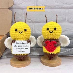 May include: Two crocheted bee figurines, one holding a red heart and the other holding a sign that reads "The influence of a good teacher can never BEE Erased!" Both bees are standing on wooden bases.