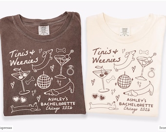 May include: Two t-shirts, one espresso and one ivory, with a graphic design. The design includes the text "Tinis & Weenies" and "Ashley's Bachelorette Chicago 2026", along with illustrations of dachshunds, martini glasses, and a disco ball.