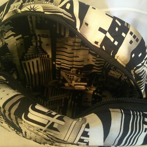 Peut inclure: Sac ouvert avec un motif g&eacute;om&eacute;trique noir et blanc et une fermeture &eacute;clair. L'ext&eacute;rieur pr&eacute;sente un design g&eacute;om&eacute;trique, tandis que la doublure int&eacute;rieure affiche une impression de paysage urbain. Le sac est ouvert, r&eacute;v&eacute;lant le design int&eacute;rieur.