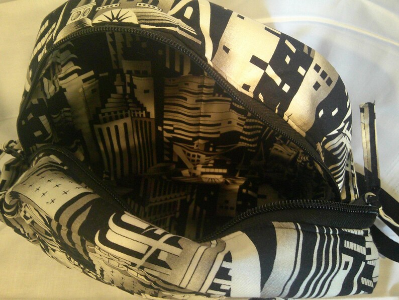 Peut inclure: Sac ouvert avec un motif g&eacute;om&eacute;trique noir et blanc et une fermeture &eacute;clair. L'ext&eacute;rieur pr&eacute;sente un design g&eacute;om&eacute;trique, tandis que la doublure int&eacute;rieure affiche une impression de paysage urbain. Le sac est ouvert, r&eacute;v&eacute;lant le design int&eacute;rieur.