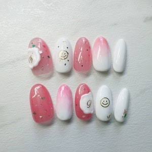 May include: Set of ten pink and white oval-shaped fake nails with various designs, including a smiley face, a flower, and glitter.