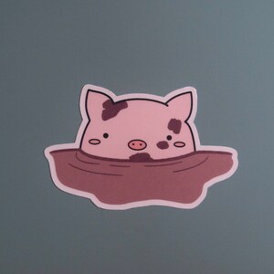 May include: A pink pig with brown spots is partially submerged in brown mud. The pig has a small pink snout and small black eyes.
