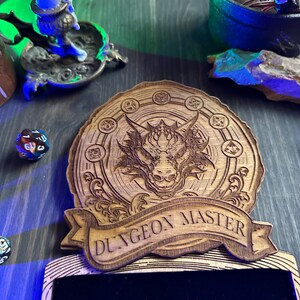 May include: A wooden plaque with a dragon design and the text "Dungeon Master". The plaque has a black velvet insert for writing.
