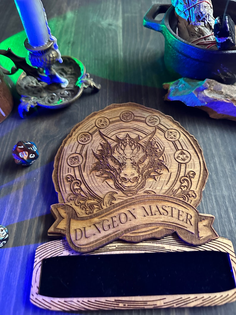 May include: A wooden plaque with a dragon design and the text "Dungeon Master". The plaque has a black velvet insert for writing.