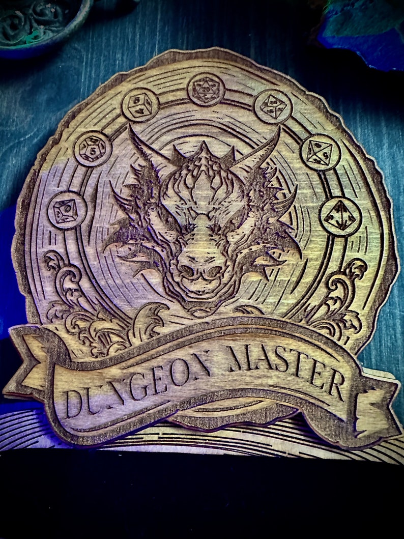 May include: A wooden plaque with a dragon design and the text "Dungeon Master" in a banner. The dragon is surrounded by a circle of dice.