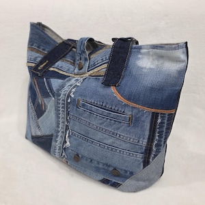 Peut inclure: Un sac fourre-tout en denim fabriqué à partir de jeans bleus recyclés. Le sac présente de multiples pièces de denim, des poches visibles et une poignée en denim. Les coutures sont visibles et le sac est de forme rectangulaire.
