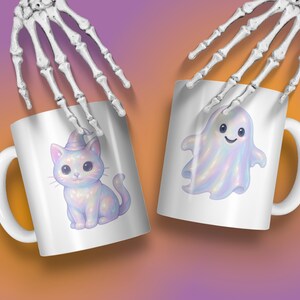 May include: Two white ceramic mugs with Halloween designs. One mug shows a cute cat in a witch's hat, the other a friendly ghost. The mugs are held by a skeleton hand against a gradient background.