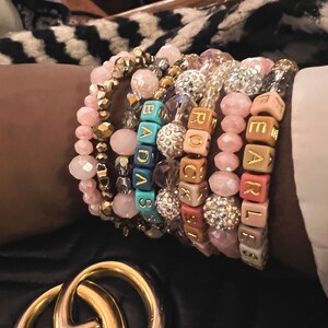 May include: A stack of colorful beaded bracelets with letter beads spelling out the words "BADASS", "ROCK", and "EARL".