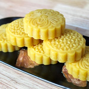 May include: Several yellow, round pastries with floral designs are arranged on a black plate. The pastries have a scalloped edge. The image presents a close-up view of the food, suggesting a dessert or snack.