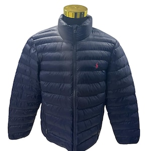 Könnte beinhalten: Eine marineblaue Steppjacke mit hohem Kragen, durchgehendem Frontreißverschluss und horizontalen Steppnähten. Ein kleines, rotes, gesticktes Logo einer Person auf einem Pferd befindet sich auf der linken Seite des Brustbereichs der Jacke.