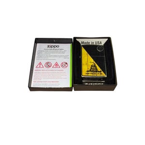 Puede incluir: Un encendedor Zippo a prueba de viento en una caja negra. El encendedor tiene un dise&ntilde;o amarillo y negro con las palabras "DON'T TREAD ON ME". La caja tambi&eacute;n contiene una etiqueta de advertencia y el texto "Made in USA".