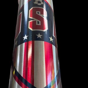 Puede incluir: Un vaso de acero inoxidable con un dise&ntilde;o patri&oacute;tico. El vaso presenta las letras "USA" en rojo, blanco y azul, junto con un gr&aacute;fico de bal&oacute;n de f&uacute;tbol y estrellas. El dise&ntilde;o incorpora rayas rojas y blancas.