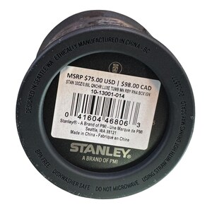 May include: Black Stanley tumbler with a white label displaying product information. The label includes the text "STANLEY" and "A BRAND OF PMI". The bottom of the tumbler has the text "BPA FREE DISHWASHER SAFE DO NOT MICROWAVE".