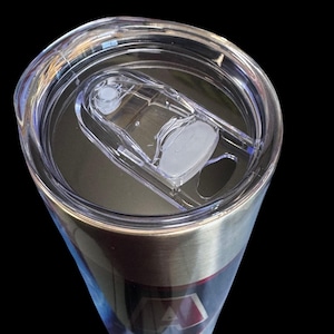 Puede incluir: Un vaso de acero inoxidable con una tapa de pl&aacute;stico transparente. La tapa tiene un cierre deslizante y una peque&ntilde;a abertura para beber. El vaso tiene una banda plateada y un dise&ntilde;o con detalles rojos y azules.