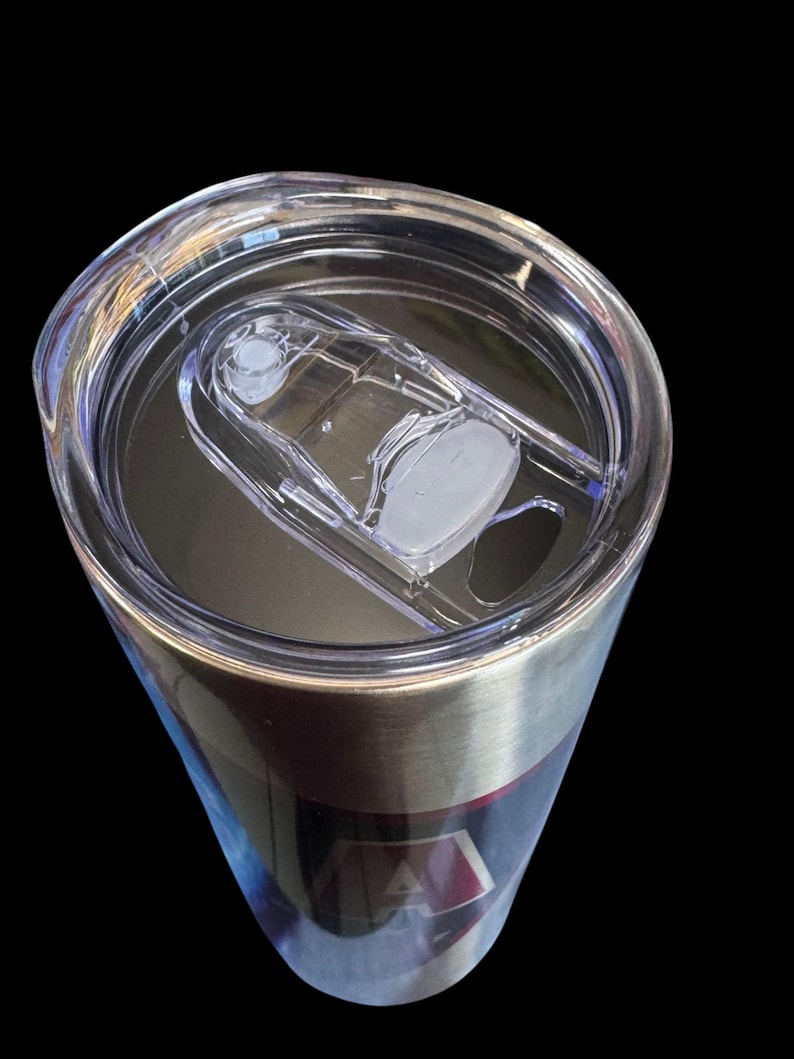 Puede incluir: Un vaso de acero inoxidable con una tapa de pl&aacute;stico transparente. La tapa tiene un cierre deslizante y una peque&ntilde;a abertura para beber. El vaso tiene una banda plateada y un dise&ntilde;o con detalles rojos y azules.