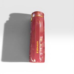 May include: A red insulated Stanley water bottle with a gold rim and the Stanley logo in gold. The bottle has a sleek, rectangular design and is likely made of stainless steel.