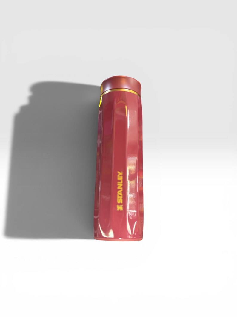 May include: A red insulated Stanley water bottle with a gold rim and the Stanley logo in gold. The bottle has a sleek, rectangular design and is likely made of stainless steel.