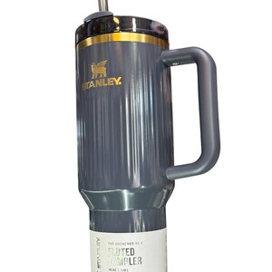 May include: A gray Stanley Quencher H2.0 Fluted Tumbler with a handle and a straw. The tumbler has a gold rim and the Stanley logo. The label reads "40 OZ | 1.18 L" and "All Day Hydration".