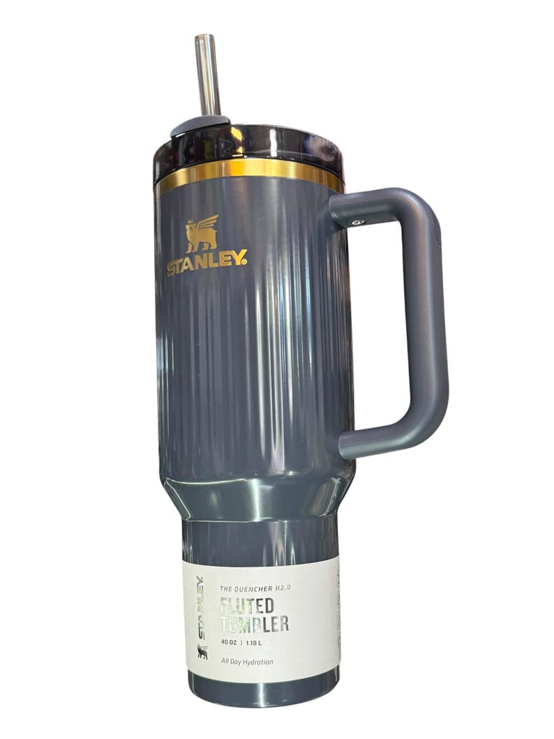May include: A gray Stanley Quencher H2.0 Fluted Tumbler with a handle and a straw. The tumbler has a gold rim and the Stanley logo. The label reads "40 OZ | 1.18 L" and "All Day Hydration".