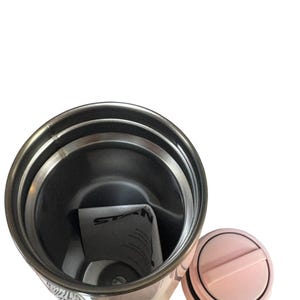 Peut inclure: Un gobelet isotherme en acier inoxydable avec un couvercle rose clair et un joint noir. Le gobelet pr&eacute;sente un motif avec du texte et des images. L'int&eacute;rieur est argent&eacute;, et un papier pli&eacute; est &agrave; l'int&eacute;rieur.