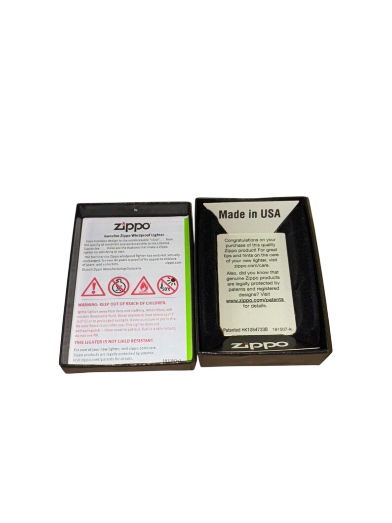 Puede incluir: Dos cajas de encendedores Zippo abiertas. Una caja muestra advertencias de seguridad y el texto "Genuine Zippo Windproof Lighter". La otra caja dice "Made in USA" e incluye el logotipo de Zippo e informaci&oacute;n del sitio web.