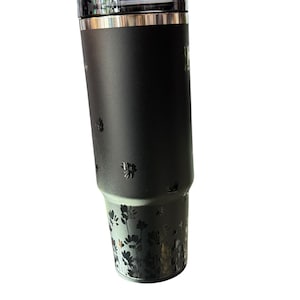 May include: A black insulated tumbler with a clear lid. The tumbler features a floral design at the bottom and small floral accents. The tumbler has a silver rim and a black handle. The tumbler is designed to keep beverages hot or cold.