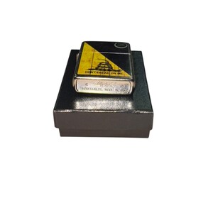 Puede incluir: Un encendedor Zippo plateado con un dise&ntilde;o negro y amarillo con la frase "DON'T TREAD ON ME". El encendedor est&aacute; sobre una caja negra. El encendedor tiene el logotipo de Zippo y el texto "BRADFORD, PA. MADE IN USA."