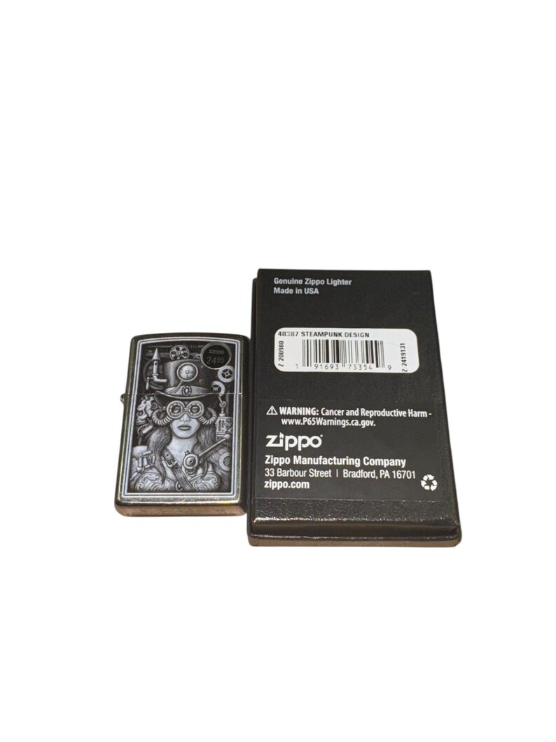 Puede incluir: Un encendedor Zippo plateado con un dise&ntilde;o steampunk que presenta a una mujer con gafas y engranajes. El encendedor est&aacute; junto a su caja negra, que incluye el texto "Genuine Zippo Lighter Made in USA".