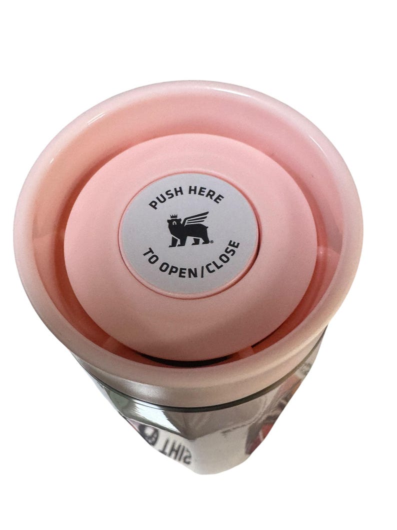 Peut inclure: Un gobelet isotherme rose avec un couvercle assorti. Le couvercle comporte un bouton circulaire avec le texte "PUSH HERE TO OPEN/CLOSE" et un dessin d'animal ail&eacute;. Le gobelet est con&ccedil;u pour garder les boissons chaudes ou froides.
