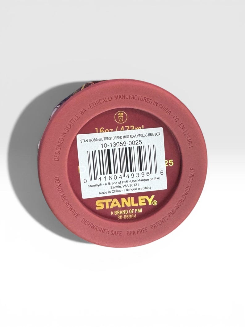 May include: A maroon-colored Stanley mug base with product information. The mug is 16oz / 473ml, dishwasher safe, and BPA free. The text includes "Designed in Seattle, WA" and "Ethically Manufactured in China."