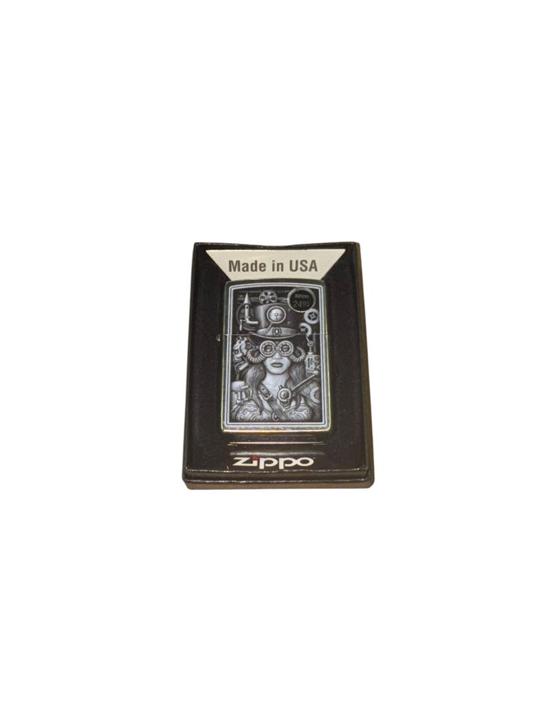 Puede incluir: Encendedor Zippo negro con un dise&ntilde;o steampunk que presenta a una mujer con gafas y engranajes. El encendedor est&aacute; en su caja original, con "Made in USA" impreso. El logotipo de Zippo es visible en la parte inferior.