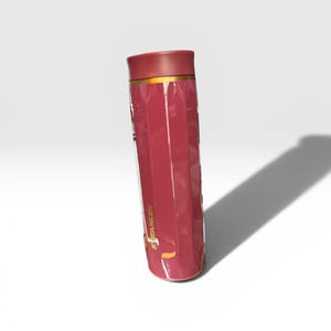May include: A maroon Stanley thermos with a gold band near the top. The thermos has a ridged design and a maroon lid. The Stanley logo is visible on the side of the thermos.